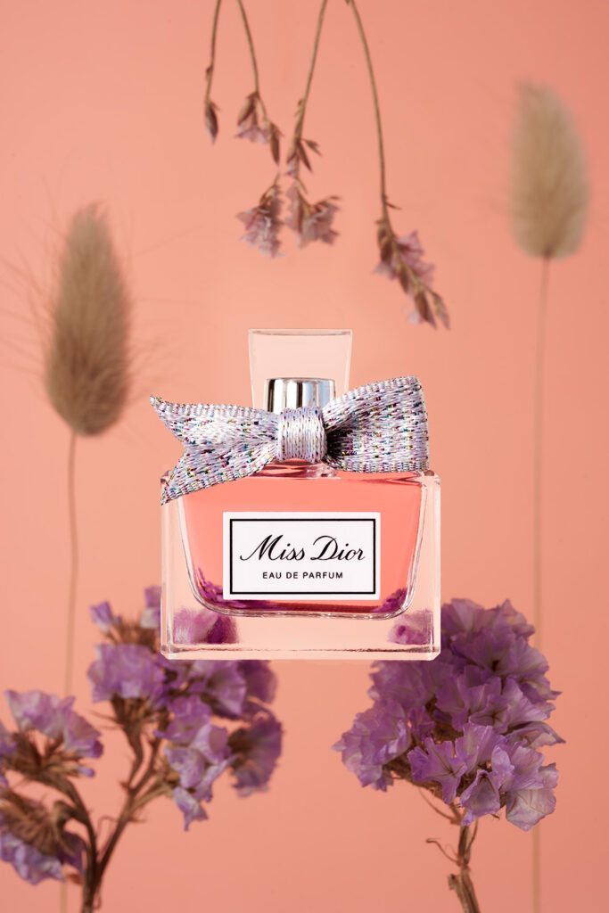 Perfume Miss Dior con flores sobre fondo rosa